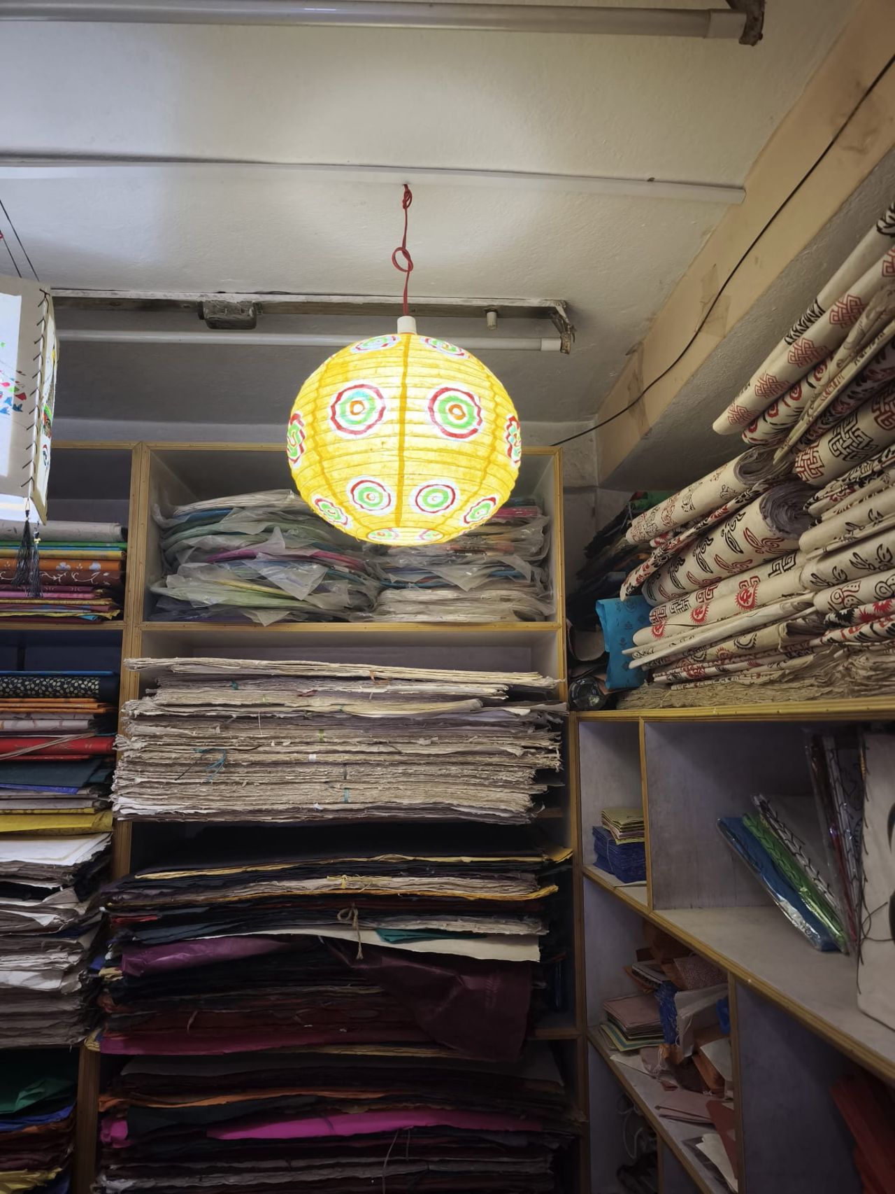 Atelier de papier Lokta à Katmandou, avec une lampe sphérique jaune éclairée au milieu des rouleaux de papier